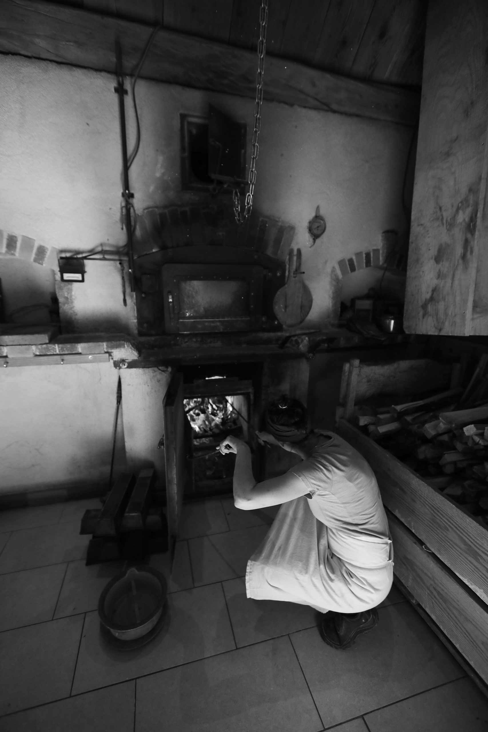 Boulangère accroupie devant un four à bois ancien